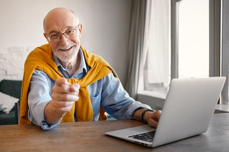 obrazek z uśmiechniętym seniorem w żółtym sweterku przed komputerem
