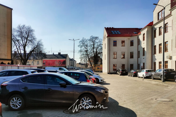 Parking przy Miejskiej Bibliotece Publicznej w Wołominie. Na zdjeciu widac budynek i zaparkowane pojazdy.