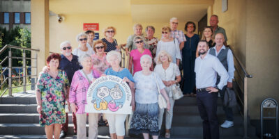 Grupa seniorów z Wołomińskiej Rady Seniorów stojąca na schodach urzędu przed wyjazdem na warsztaty